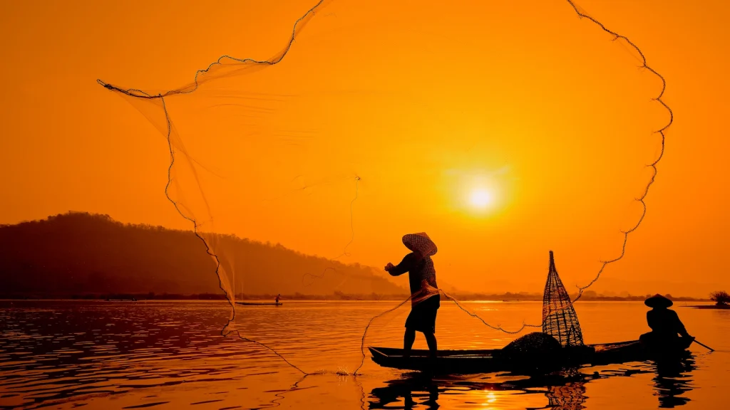 Due uomini su una barca da pesca nel fiume Mekong al sorgere del sole | Tour Vietnam, viaggi di gruppo esclusivi Alidays