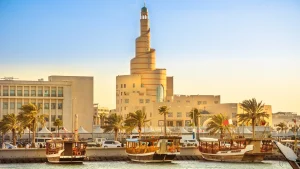 Tradizionale dhow in legno ancorato nel porto di Dhow nella baia di Doha, con moschea a spirale e minareto sullo sfondo al tramonto. Qatar, Medio Oriente.