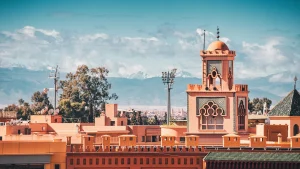 Architettura tradizionale marocchina con minareto e le montagne dell'Atlante che si ergono sullo sfondo a Marrakech, in Marocco
