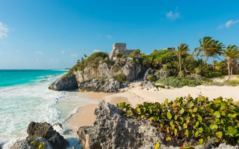The Caribbean Sea with turquoise waters and white sand beach as a backdrop for the Tulum Maya ruins, Mexico.