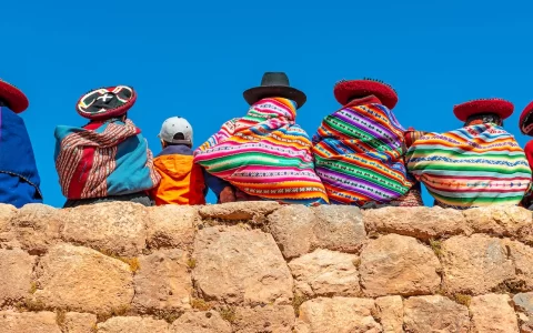 Fotografia panoramica di donne indigene quechua in abiti tradizionali con un ragazzo seduto su un antico muro inca a Chinchero, provincia di Cusco, Perù.