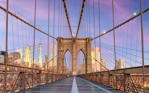 New York on the Brooklyn Bridge Promenade facing Manhattan's skyline at dawn.