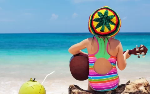 happy baby in rastaman hat have fun, play reggae music on Hawaiian guitar