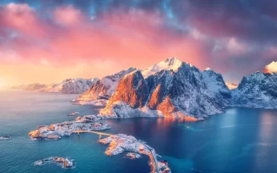 Beautiful landscape with blue sea, snowy mountains, rocks and islands, village, rorbu, road, bridge and pink sky at sunrise. Aerial view. Hamnoy in snow in winter in Lofoten islands, Norway.