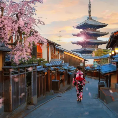 Kyoto al tramonto con la pagoda Yasaka, una giovane donna giapponese in kimono tradizionale, la fioritura dei ciliegi al culmine e petali di sakura